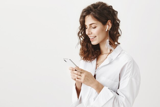 Stylish successful businesswoman using mobile phone and wireless earphones