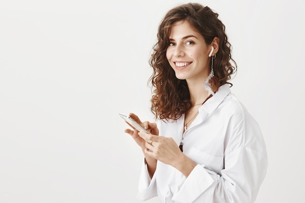 Stylish successful businesswoman using mobile phone and wireless earphones