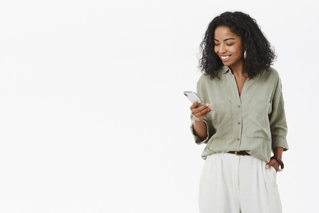 Stylish and successful dark-skinned female african entrepreneur checking smartphone smiling
