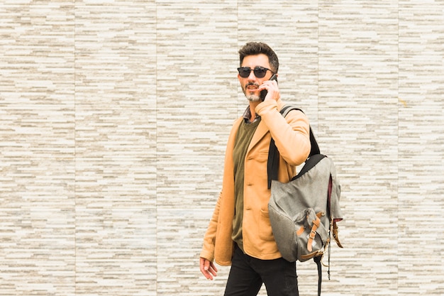 Free photo stylish traveler standing against wall talking on mobile phone