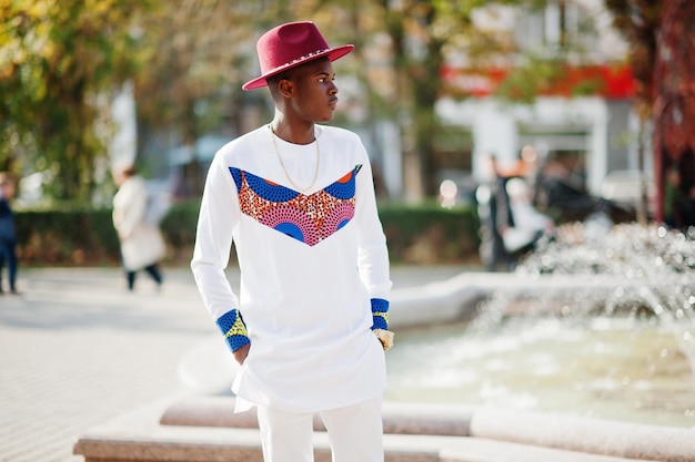 秋の日にポーズをとった赤い帽子と白い服を着たスタイリッシュなトレンディなアフロフランスの男黒人アフリカ系モデルの男