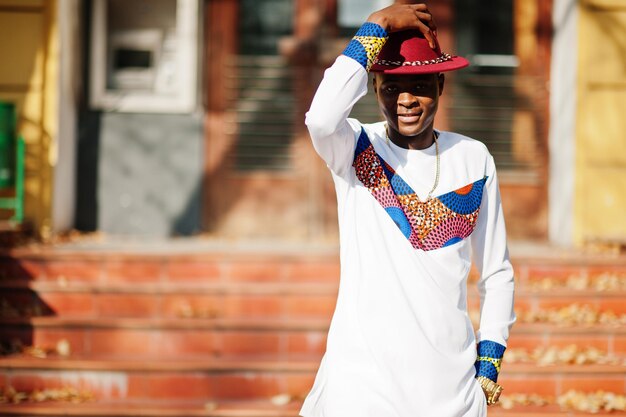 Стильный модный афро-француз в красной шляпе и белом наряде позирует в осенний день