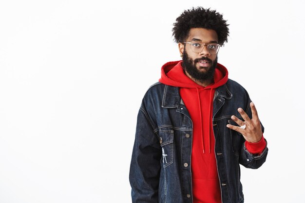 Stylish urban goodlooking african bearded guy with afro hairstyle and piercing in glasses showing number four with fingers and looking at camera awaiting order or talking about forth place
