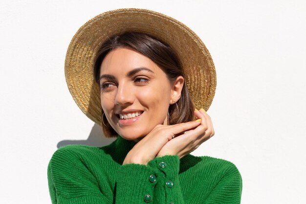 Stylish woman in green casual sweater and hat outdoor on white wall calm and confident smile