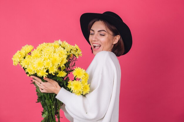 Stylish woman in hat and casual white sweater on pink red wall