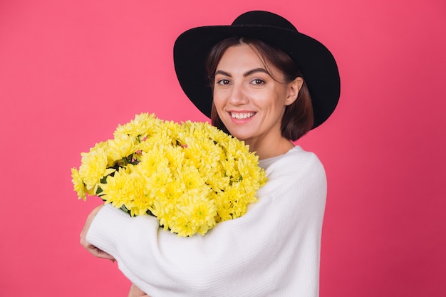 Stylish woman in hat and casual white sweater on red wall