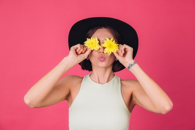 Free photo stylish woman in hat, send air kiss cover eyes with yellow asters, spring mood, happy emotions isolated space
