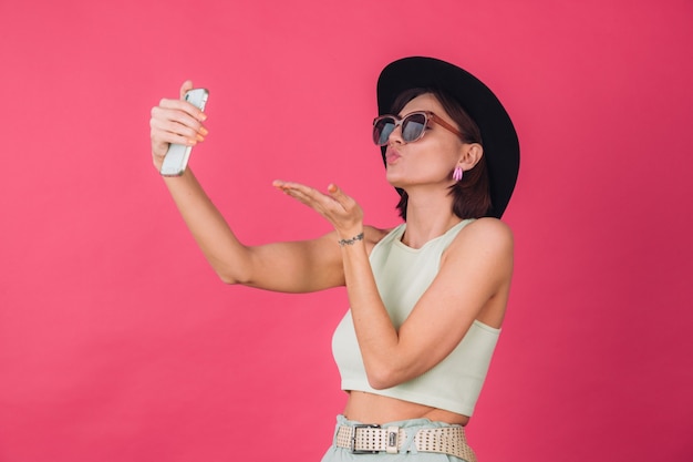 Stylish woman in hat and sunglasses on pink red wall