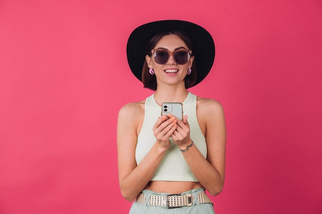 Stylish woman in hat and sunglasses on pink red wall