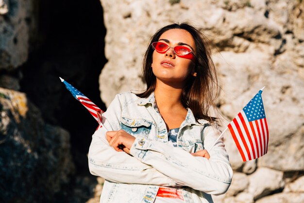 Stylish woman holding little US flags on rocks