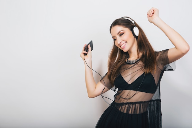 stylish woman isolated in black suit listening to music on headphones dancing