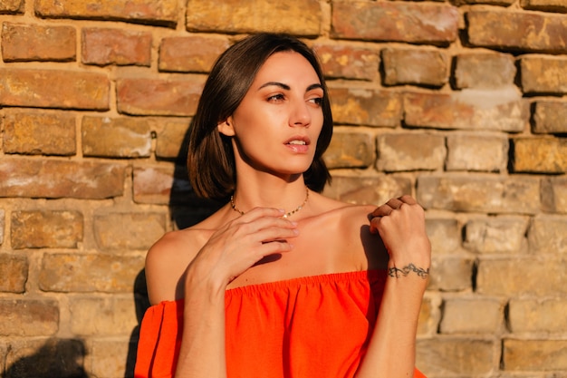 Stylish woman in orange clothes at sunset at brick wall