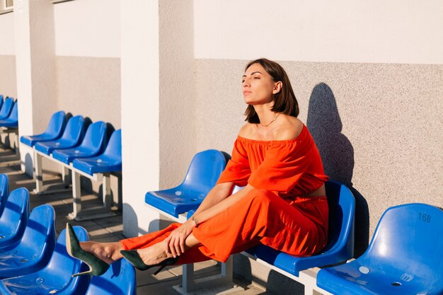 Stylish woman in orange clothes at sunset at cycle track stadium posing