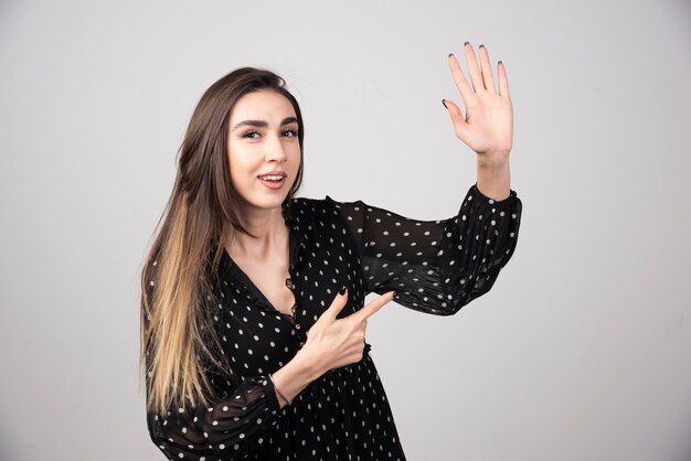 Stylish woman pointing at her hand on gray.