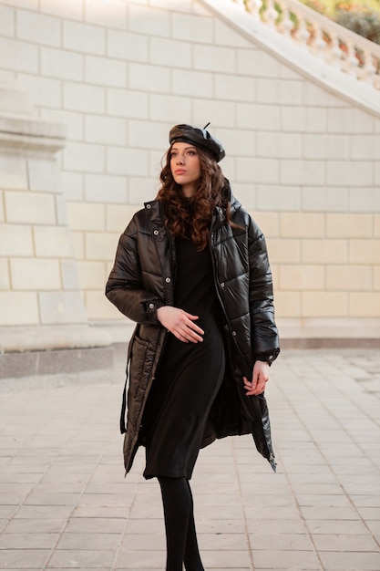 無料写真 冬の秋のファッショントレンドでポーズをとるスタイリッシュな女性ハイヒールの靴を履いて古い美しい通りで黒のフグコートと革の帽子のベレー帽
