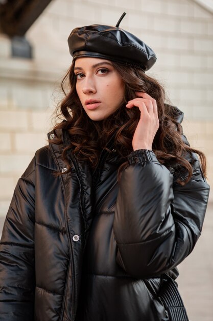 stylish woman posing in winter autumn fashion trend black puffer coat and leather hat beret in old beautiful street wearing high heel shoes