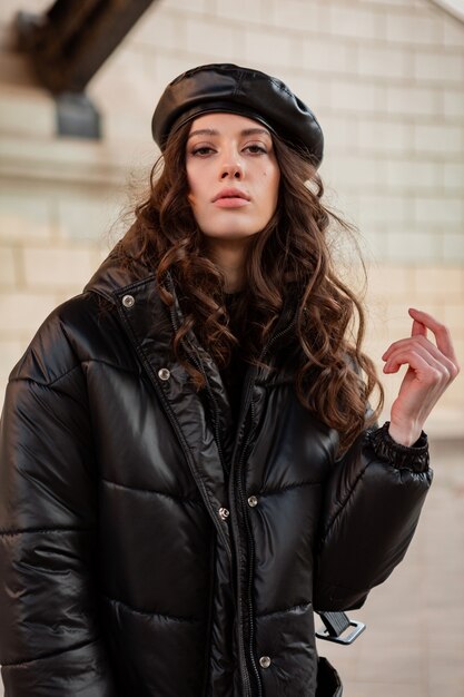 stylish woman posing in winter autumn fashion trend black puffer coat and leather hat beret in old beautiful street wearing high heel shoes