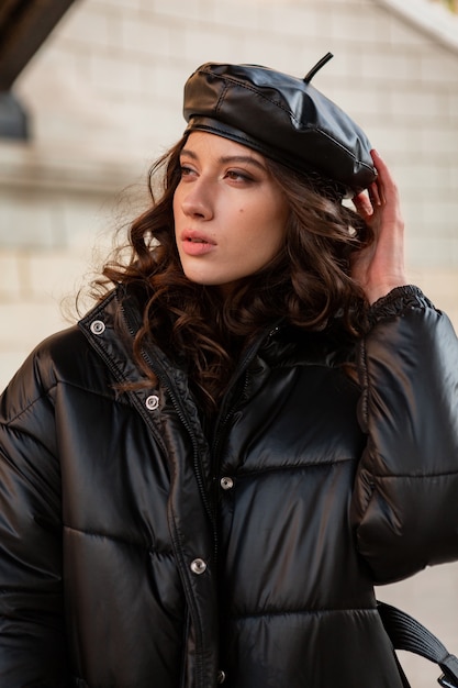 Stylish woman posing in winter autumn fashion trend black puffer coat and leather hat beret in old beautiful street