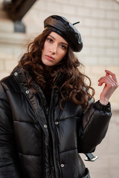 Stylish woman posing in winter autumn fashion trend black puffer coat and leather hat beret in old beautiful street