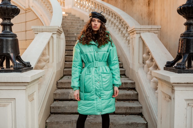 Stylish woman posing in winter autumn fashion trend blue puffer coat and hat beret in old beautiful street stairs