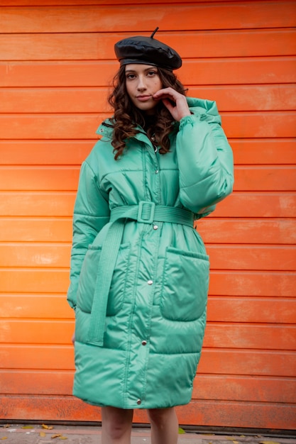거리에서 오렌지 벽에 겨울 가을 패션 트렌드 호흡기 코트와 모자 베레모 포즈 세련된 여자