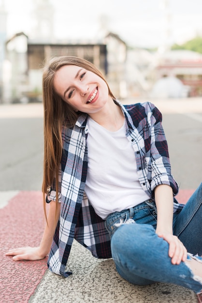 Foto gratuita donna alla moda che si siede sulla strada che guarda l'obbiettivo