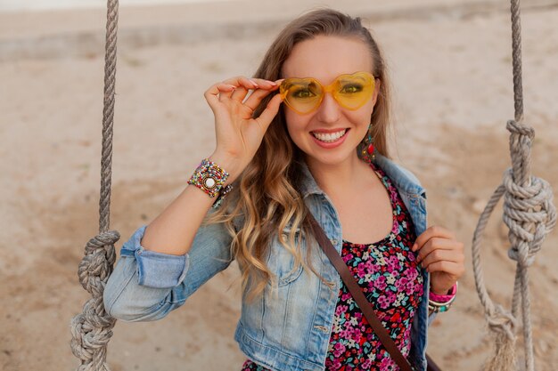 Stylish woman in summer dress vacation on beach in colorful yellow sunglasess smiling happy