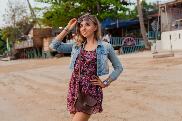 Stylish woman in summer dress vacation walking on beach with sunglasses