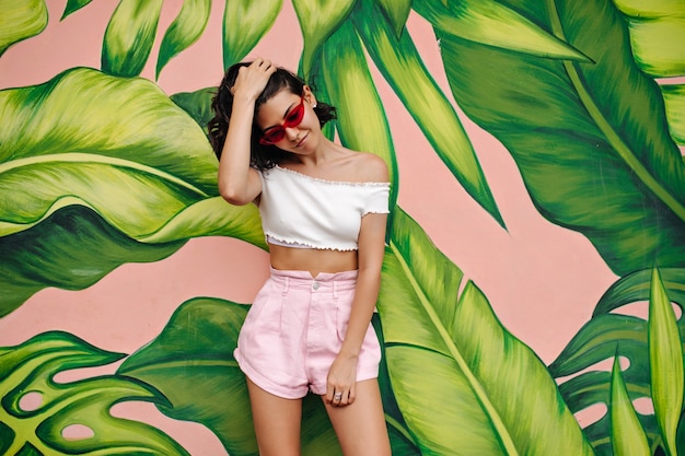 Stylish woman in summer outfit posing near graffiti