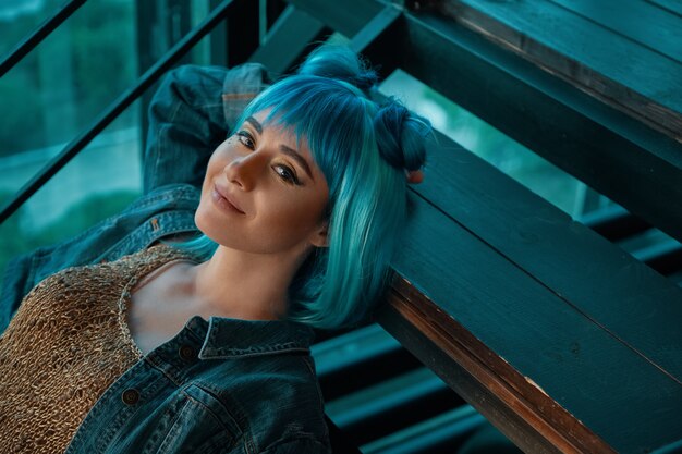 Stylish woman wearing a blue wig laying on stairs
