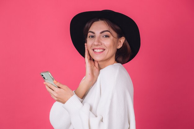 Stylish woman in white casual sweater and hat on red pink wall