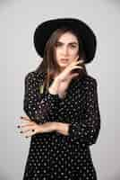 Free photo stylish woman with black hat standing on gray.