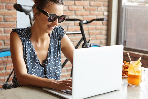 Stylish woman with charming smile sitting in front of open laptop, enjoying online communication