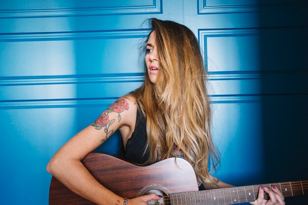 Stylish woman with guitar near blue wall