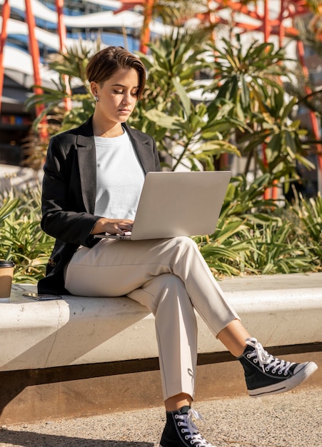 Стильная женщина, работающая на ноутбуке на открытом воздухе