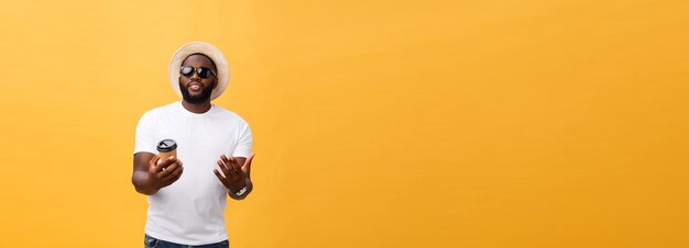 Stylish young african american man holding cup of take away coffee isolated over yellow background