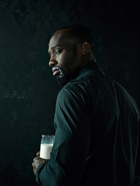 Стильный молодой африканский черный человек с белой чашкой кофе позирует на темном фоне студии.