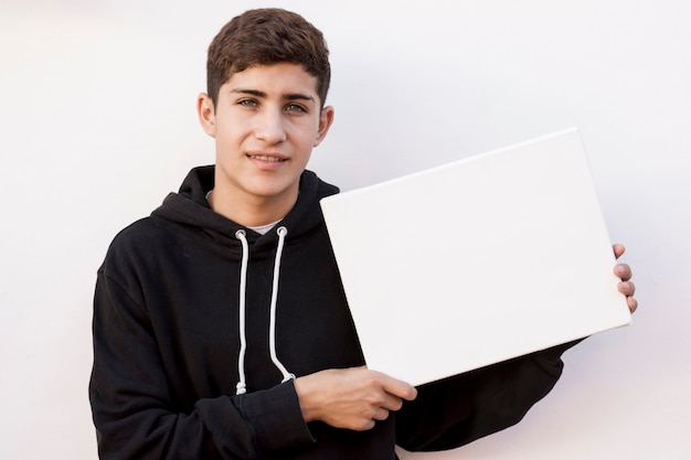 Stylish young boy holding blank white placard against white wall