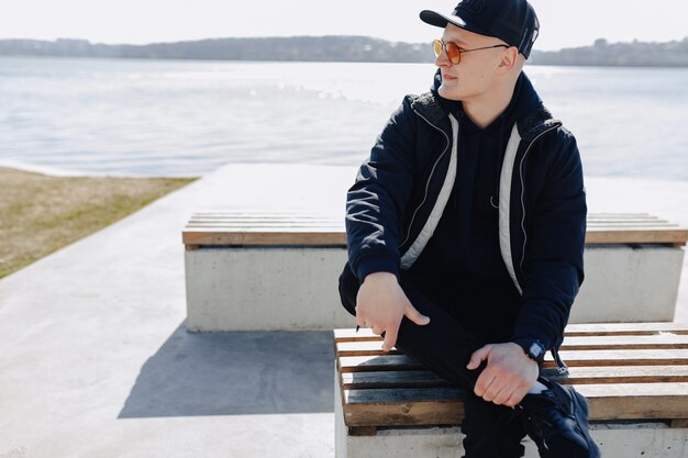 Stylish young boy in orange glasses, jacket and cap, walk around the lake in spring or autumn