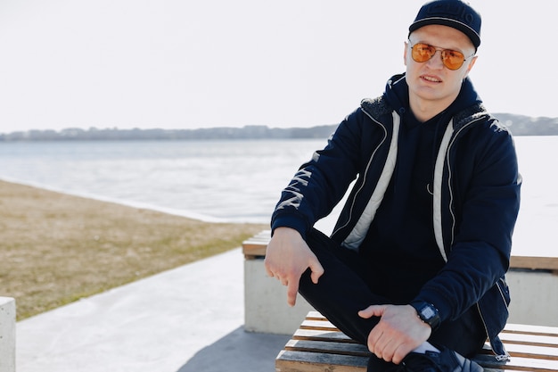 Stylish young boy in orange glasses, jacket and cap, walk around the lake in spring or autumn