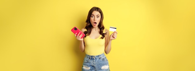 Free photo stylish young brunette woman holding credit card and smartphone paying purchase or order something i