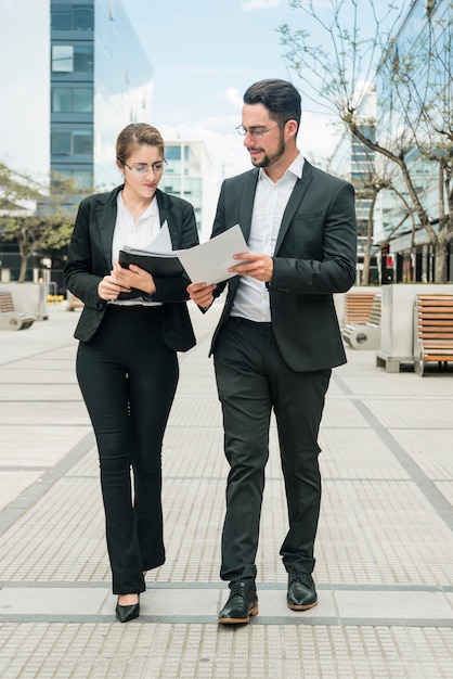 Free photo stylish young businessman and businesswoman looking at document while walking on the pavement