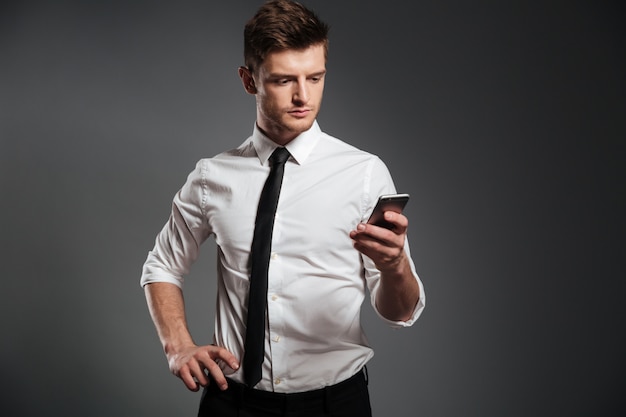 Stylish young businessman using mobile phone while standing