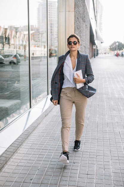 Stylish young businesswoman walking on sidewalk