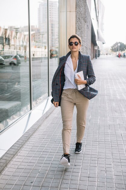 Stylish young businesswoman walking on sidewalk