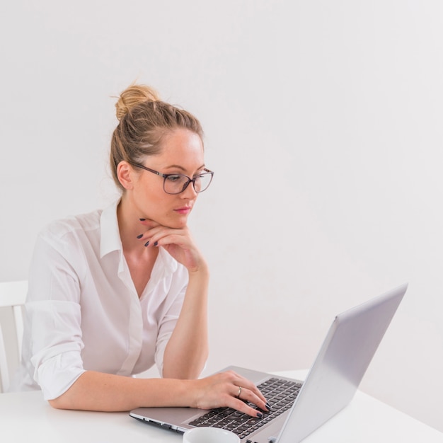 Stylish young businesswoman wearing eyeglasses looking at laptop