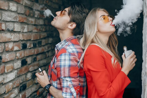 Stylish young couple with vape in a city