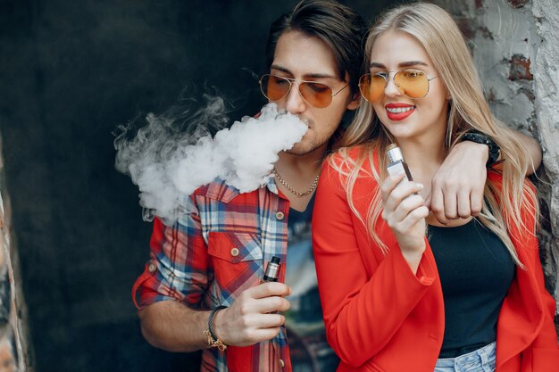 Stylish young couple with vape in a city