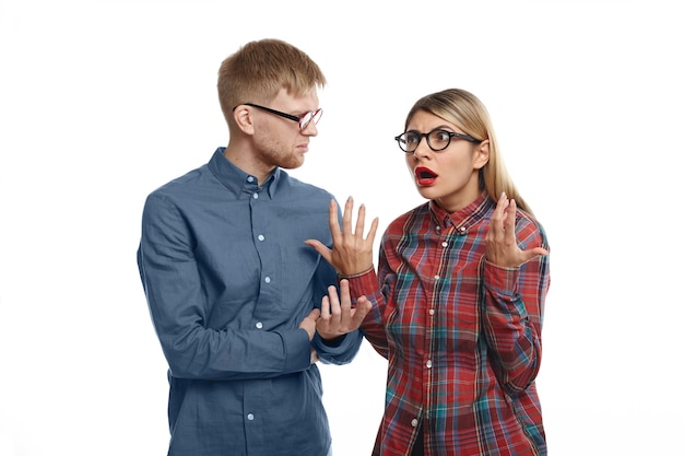 Stylish young European couple in glasses having arguement: emotional blonde girl with fed up look, feeling tired and stressed while explaining her grumpy bearded husband thar she is right