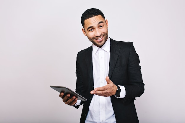 Stylish young handsome man in white shirt, black jacket, with tablet smiling. Achieve success, great work, expressing true positive emotions, businessman, smart worker.